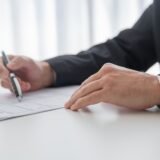 Semnarea unui antecontract imobiliar cu stiloul, pe o masă de birou, alături de documente