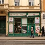 Vitrine de magazine la parterul unor clădiri, cu trecători pe trotuarul unei străzi comerciale