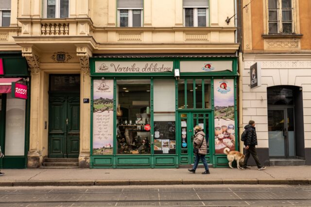 Vitrine de magazine la parterul unor clădiri, cu trecători pe trotuarul unei străzi comerciale