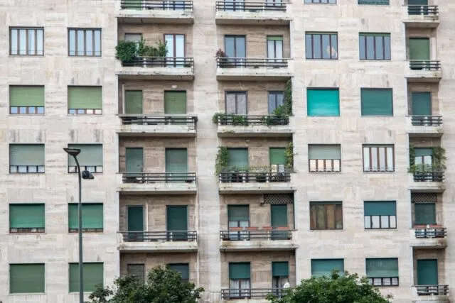 Fațada unui bloc de locuințe cu balcoane, văzută de jos, într-o după-amiază senină